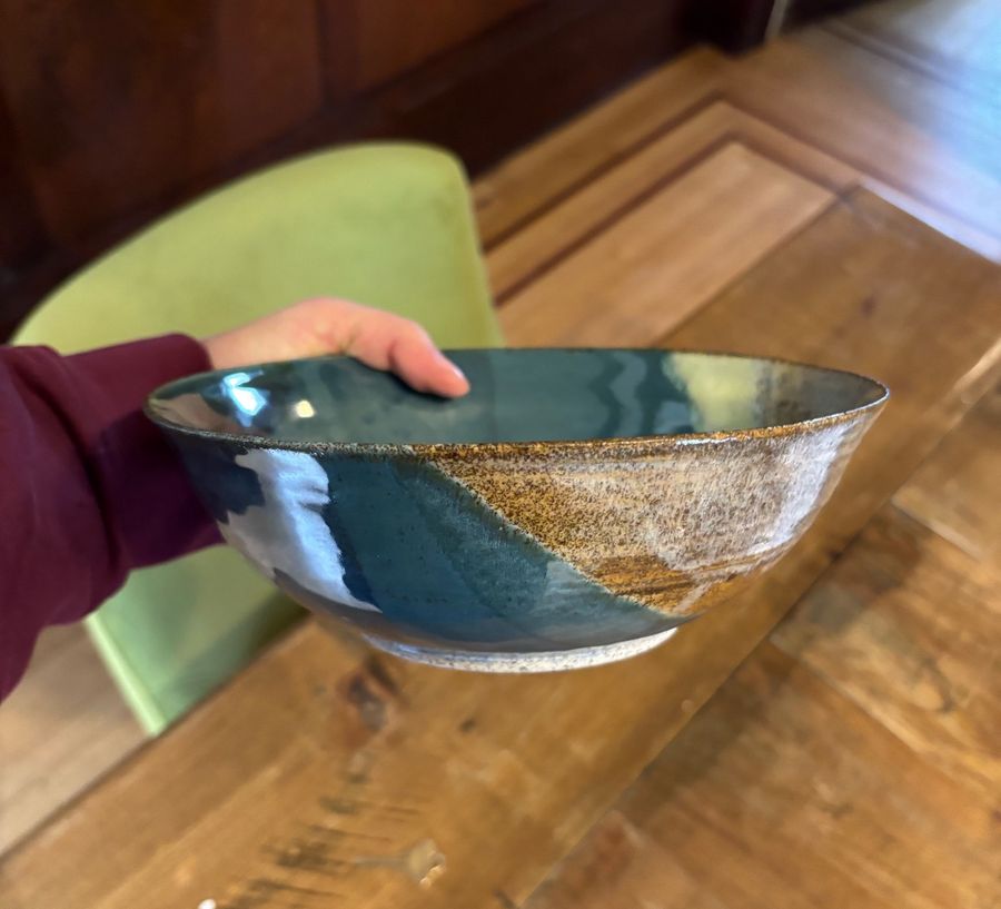 Layered bowl — a large bowl held over a wooden table, deep teal glaze giving way to speckled tan and cream