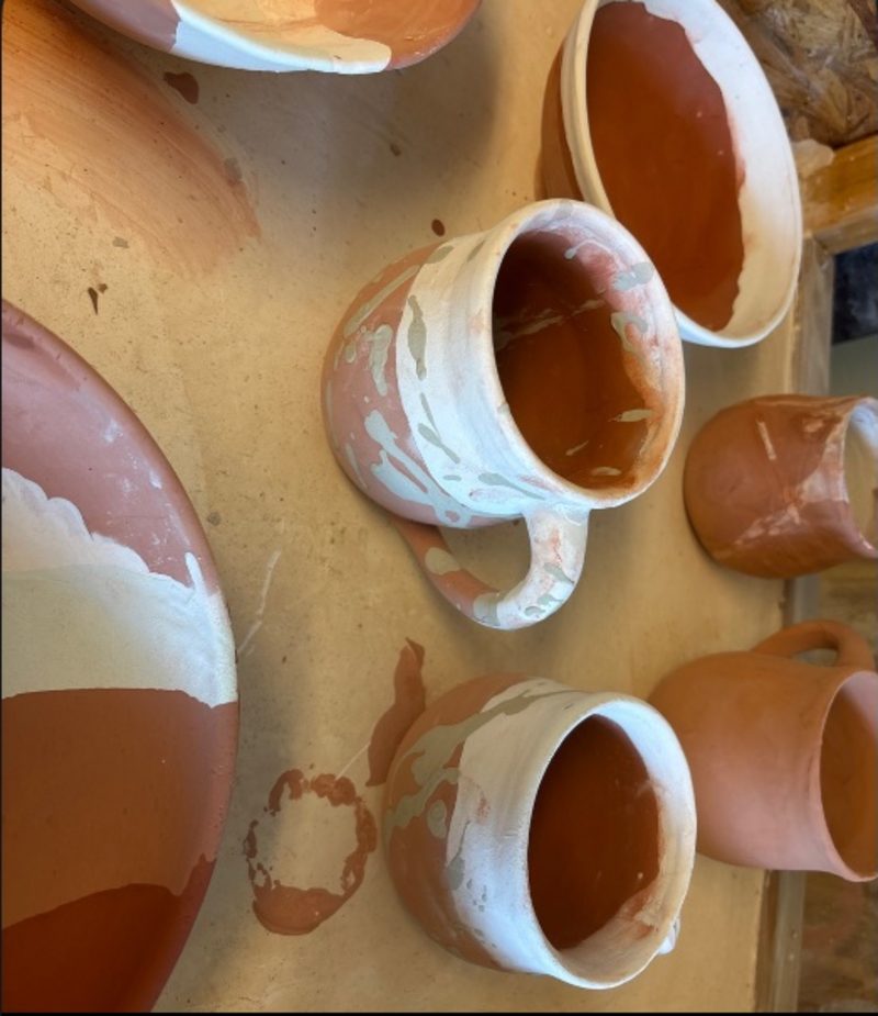 Cosmic 3 — a group of bisqued mugs and a bowl, mid-glaze, on the board