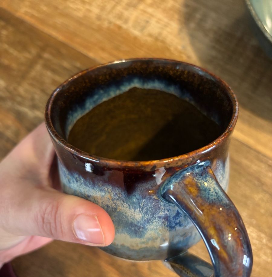 Cosmic mug — a handmade mug held in one hand, dark rim over layered blue, brown and cream glaze