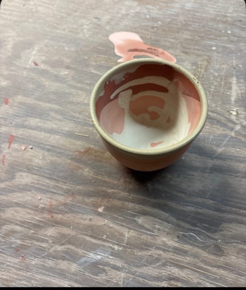 Untitled — a small bisqued cup on the wooden table, slip swirled inside it