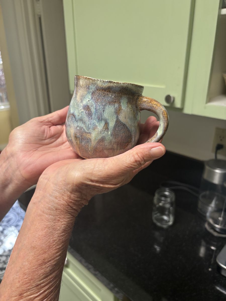 A handmade mug in mottled blue-green-brown glaze, held up in two hands