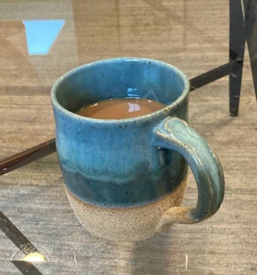 aqua and cream mug, fired — blue over speckled clay, filled, on a glass table