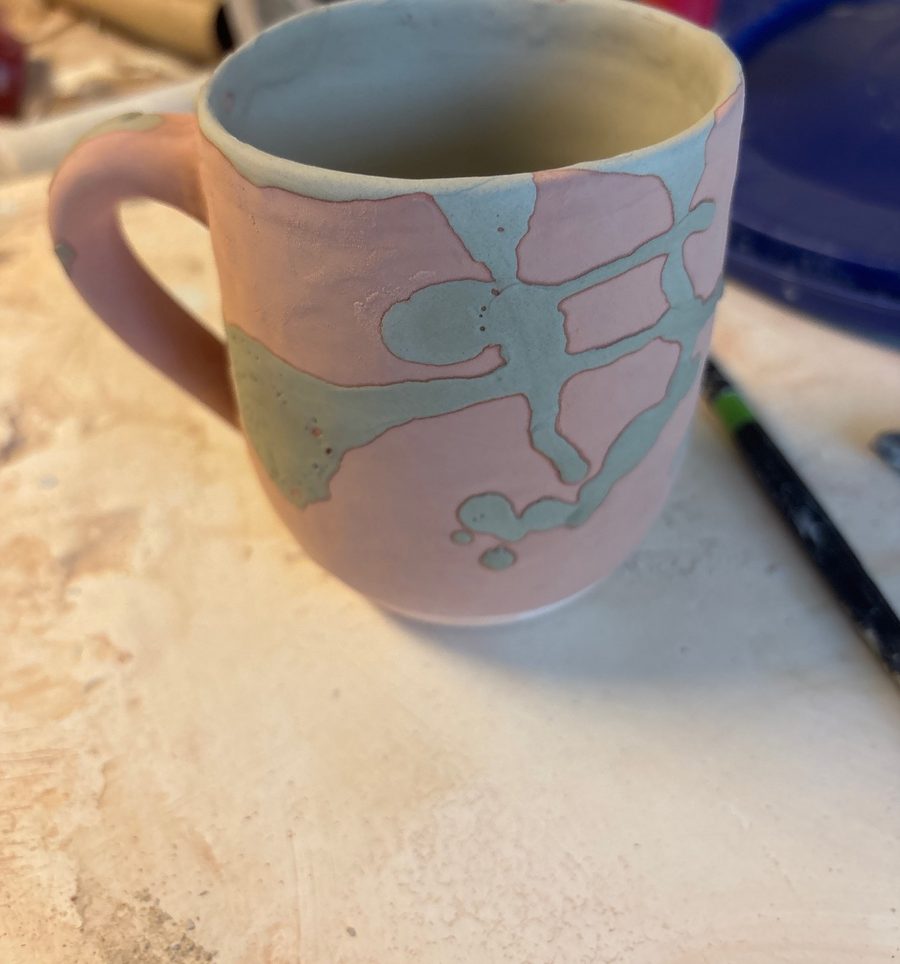 Seafoam mug, unfired — pink clay with swoops of seafoam and cream, on the bench
