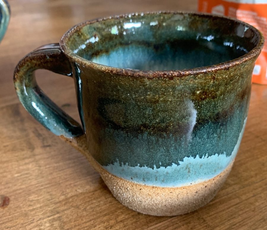 bluegreen with cream inside — deep blue-green glaze over speckled clay, on a wooden table